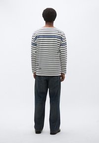 Μπλουζάκι με μακριά μανίκια και ρίγες σε ναυτικό και ανοιχτό γαλάζιο, κατασκευασμένο από βαμβάκι. Συνδυάζεται με άνετο σκούρο τζιν και μαύρα παπούτσια.