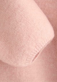 Miękka, różowa dzianina z bliskim ujęciem mankietu, ukazującym delikatną, puszystą teksturę i ściągacz na krawędzi.