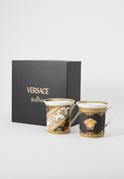 Πορσελάνινα φλυτζάνια Versace σε μαύρο και λευκό, διακοσμημένα με χρυσά μοτίβα, με λεπτομέρεια κεφαλής Μέδουσας, παρουσιάζονται σε μαύρο κουτί.
