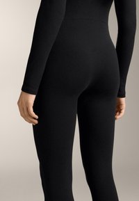 Colanți negri dintr-un material neted și elastic. Design ajustat cu mâneci lungi, având spatele fără cusături și o siluetă curată, simplă.