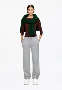 Dark brown long-sleeve top, gray sweatpants with drawstring, and a green knitted scarf draped around the neck. White sneakers.
