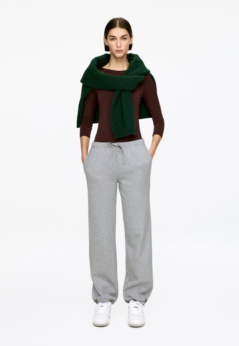 Dark brown long-sleeve top, gray sweatpants with drawstring, and a green knitted scarf draped around the neck. White sneakers.