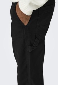 Pantaloni cargo neri, in tessuto di cotone, con tasche laterali, cuciture a vista, gamba leggermente affusolata, con superficie strutturata e senza motivi visibili.