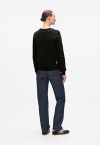Svart bomullssweater med ribbede mansjetter, parret med mørkeblå denimjeans med rett ben og kontraststing. Svart sneakers med hvite detaljer.