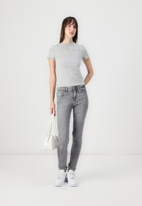 Gray short-sleeve t-shirt, fitted design, paired with light gray skinny jeans. Model carries a white bag and wears white sneakers.