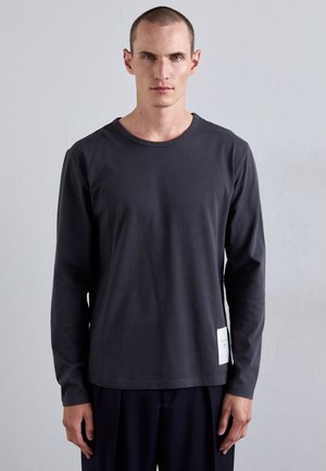 Tumedateh grey pikka varrukat shirt puuvillast, ümmarguse kaelusega ja väikese valge sildiga vasakul küljel hemmi lähedal. Ühtlane tekstuur.