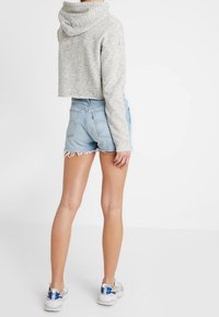 Šedá zkrácená mikina s kapucí, doplněná světlemodrými džínovými šortkami s třepenými okraji. Na nohou světlé sportovní boty.