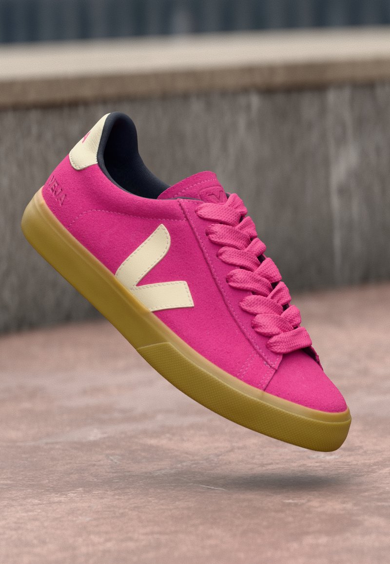 Růžová semišová teniska s krémovým logem, plochými tkaničkami a žlutou gumovou podrážkou. Má zaoblenou špičku a polstrovaný lem pro pohodlí.