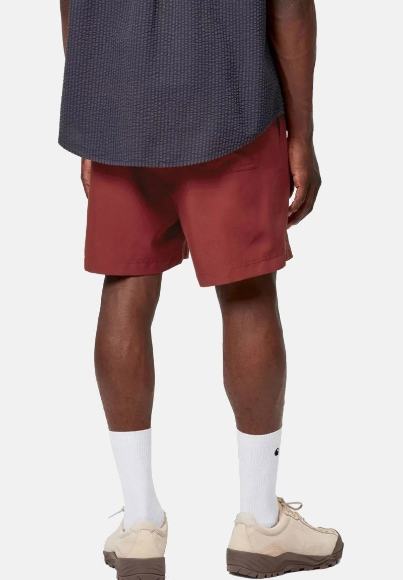 Mann mit dunkelblauem, strukturiertem Hemd, bordeauxroten Shorts, weißen Socken und beigen Sneakers, steht mit dem Rücken zum Betrachter.