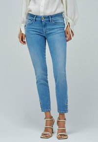 Jeans de denim azul claro con un corte slim, que presentan un cierre de botón, bolsillos frontales y botones decorativos en el dobladillo recortado.