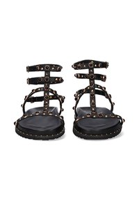 Sandalias negras con tiras, con múltiples tiras horizontales, detalles de tachuelas y suela plana. Presenta tachuelas doradas a lo largo de los bordes.