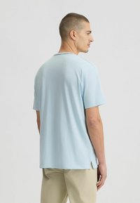 Camicia azzurra chiara a maniche corte con collo rotondo, fessure laterali all'orlo, superficie liscia e vestibilità leggermente rilassata.