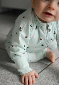 Ljust grön babybody med dragkedja, prydd med olika färgglada insekter i ett lekfullt mönster. Mjuk tygkvalitet och tight passform.