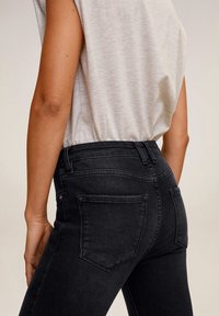 Schwarze, hoch taillierte Jeans aus Denim mit glatter Textur. Sie verfügen über zwei Gesäßtaschen und dezente Nähte.