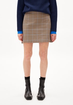 Bruine geruite rok met blauwe accentlijnen, gestructureerde stof, rechte snit boven de knie, gecombineerd met zwarte enkelboots en een marineblauw vest.