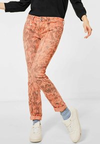 Korallmönstrade jeans med smal passform, med uppvikta fållar och kontrasterande brunt mönster. I kombination med vita sneakers och ljusblå strumpor.