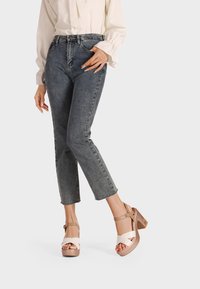 Sandali platform beige con cinturini incrociati color crema, dotati di tacco grosso. Indossati con jeans blu a vita alta.