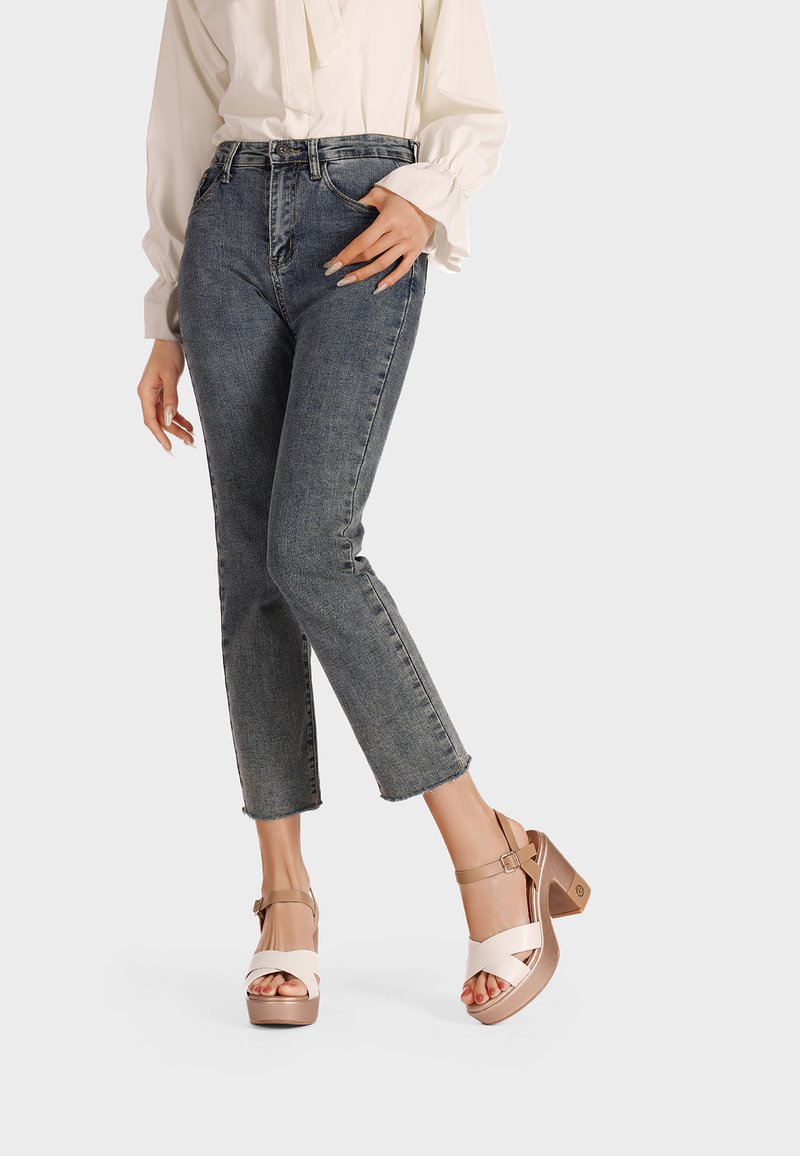 Sandali platform beige con cinturini incrociati color crema, dotati di tacco grosso. Indossati con jeans blu a vita alta.