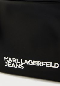 Czarna nylonowa torba o gładkiej fakturze, z białym wypukłym logo "KARL LAGERFELD JEANS". Prosty, prostokątny kształt bez dodatkowych ozdób.