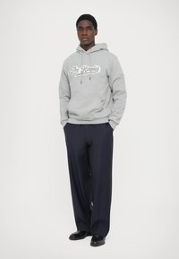 Sweat à capuche gris avec cordons de serrage et poche avant, comportant du texte blanc. Associé à un pantalon rayé bleu marine et des chaussures noires. Coupe standard.