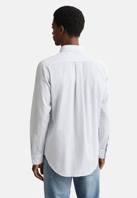 Hellblau gestreiftes Hemd mit Button-Down-Kragen, langen Ärmeln und abgerundetem Saum. Verfügt über ein vertikales Streifenmuster und eine Rückenpasse.