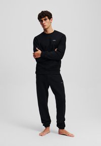 Completo in cotone nero composto da felpa e pantaloni della tuta, con scollatura tonda, polsini a coste e un piccolo logo sul petto e sui pantaloni.