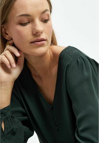 Blusa verde scuro con scollatura a V, tessuto morbido e dettagli delle maniche plissettati. Presenta una chiusura con bottoni sul davanti e una vestibilità rilassata.