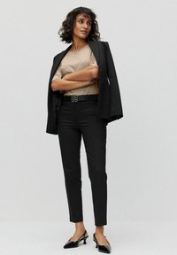 Svart skräddarsydd kavaj, beige topp, svarta byxor och svarta slingback-hälar. Designad med en glänsande fjärilsbälte, släta tygtexturer.