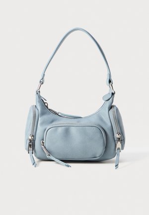 Light blue leather handbag with a rounded shape, two zippered pockets, a short handle, and silver hardware accents. Smooth texture.