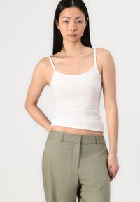 Top in cotone bianco senza maniche con spalline sottili, design aderente, texture liscia, abbinato a pantaloni verdi su misura con gamba dritta e davanti piatto.