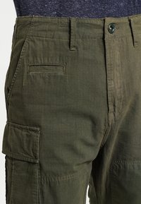 Olivgrön cargobyxor med en texturerad tyg, som har sid- och bakfickor samt knappstängning.