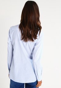 Long-sleeve, light blue button-up shirt with vertical white stripes, made of a smooth fabric. Includes button cuffs and a curved hem.