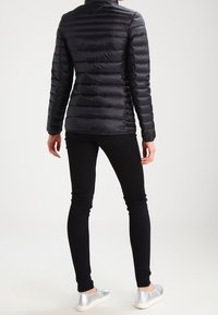 Svart puffjacka med horisontell quiltad design, ståkrage och en kompakt passform, parat med slim-fit svarta byxor och silverfärgade slip-on skor.