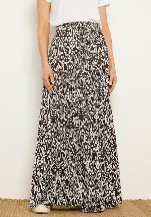 Kobieta ubrana w długą spódnicę z czarno-białym zwierzęcym wzorem, związaną w pasie, w połączeniu z białym T-shirtem i białymi butami.