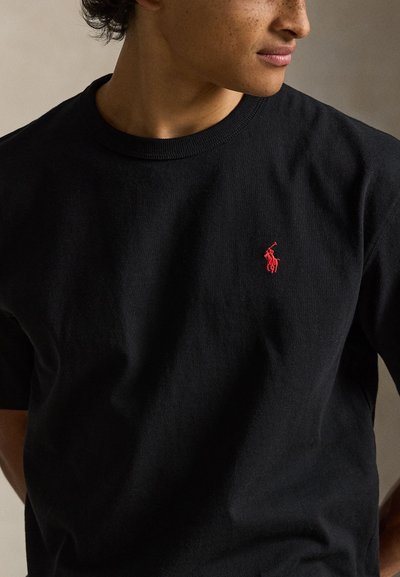 Μαύρο βαμβακερό T-shirt με κοντά μανίκια, με μικρό κόκκινο κεντητό έμβλημα στο αριστερό στήθος. Κλασικός στρογγυλός γιακάς.