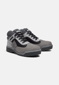 Grijze en zwarte wandelschoenen van suede en mesh materialen, rubberen zool, vetersluiting, gevoerde kraag en een logosticker aan de zijkant.