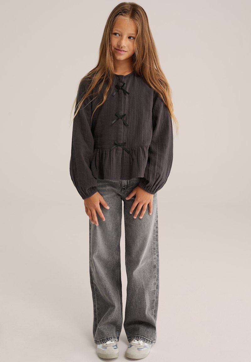 Svart texturerad blus med puffärmar, prydd med satinband. I kombination med vida grå denimjeans och ljusa sneakers.