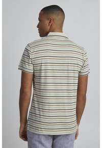 Kortermet polo skjorte med horisontale striper i svart, brunt og lys beige på en lys grønn bakgrunn; laget av bomull.