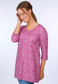 Pink tunic with a floral pattern, V-neck, and three-quarter sleeves, made of soft fabric, slightly loose fit, worn with blue jeans.