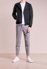 Giubbotto bomber nero texture con dettagli argentati sulla zip, abbinato a pantaloni grigi chiari a gamba affusolata e sneakers bianche. Maglietta bianca a girocollo semplice.