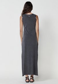 Vestido maxi gris sin mangas con un top ajustado y una falda suelta. Presenta una tela texturizada, aberturas laterales y un ribete estampado en el escote.
