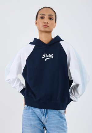 Temno modra kapuca z belimi in svetlo modrimi raglan rokavi. Poudarjen napis 'Pariz' v pisavi. Tkanina se zdi mehka in teksturirana.