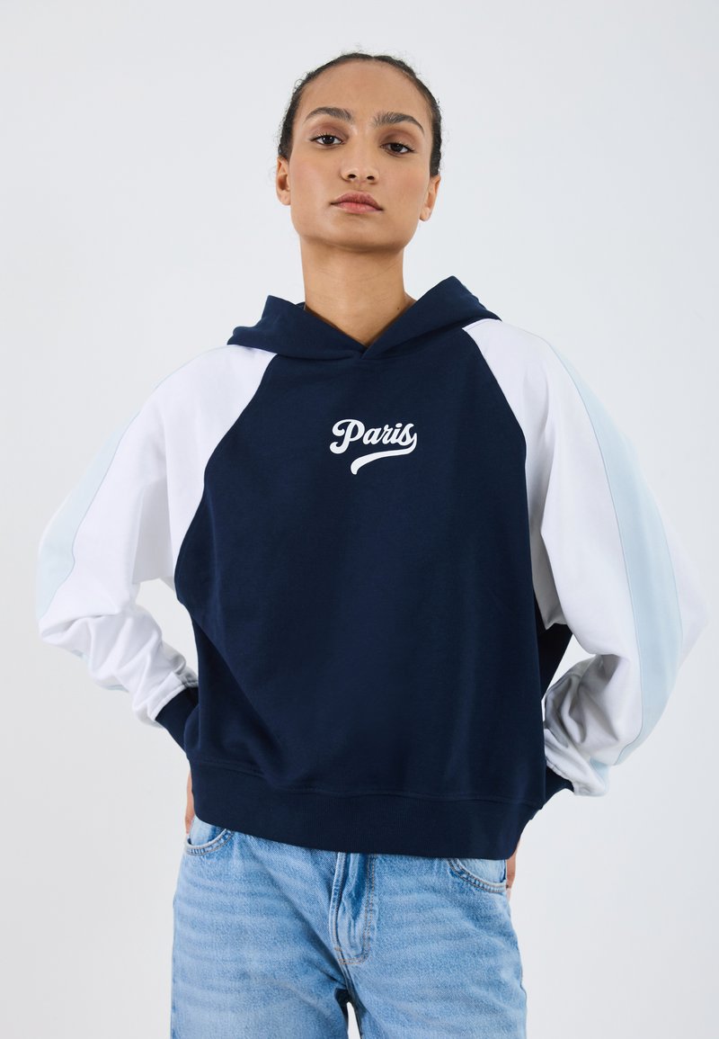 Hoodie blu navy con maniche raglan bianche e azzurro chiaro. Presenta una grafica con la scritta 'Paris'. Il tessuto sembra morbido e texturizzato.