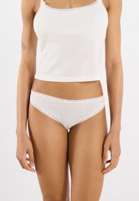 White cotton crop top and matching thong, featuring ribbed texture and lace trim. The design includes a delicate pattern on the underwear.
