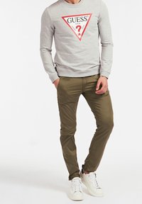 Szary sweatshirt z czerwonym trójkątnym logo i napisem, zestawiony z oliwkowymi spodniami oraz białymi trampkami z czarnymi akcentami.
