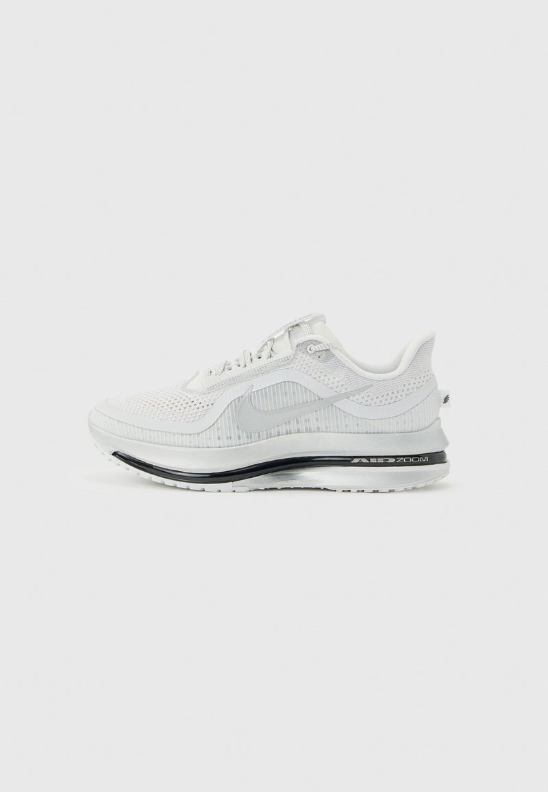 Λευκό αθλητικό παπούτσι Nike Air Zoom με πλεκτό επάνω μέρος, γκρι λογότυπο swoosh και μαύρη επένδυση στην σόλα, σε ανοιχτό γκρι φόντο.