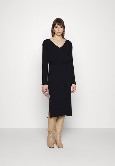 Strikkjole i mørk navy, V-hals, lange ærmer, bælte i taljen, sidelæg, parret med knæhøje beige støvler og en multicolor clutch.