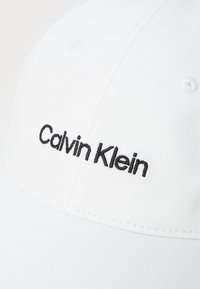 Căciulă de baseball albă, din bumbac, cu un design structurat. Prezintă un logo brodat în negru "Calvin Klein" pe panoul din față.