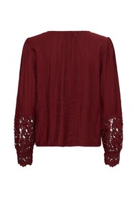Blouse à manches longues rouge foncé en tissu texturé avec des découpes en dentelle florale aux poignets, vue de dos.