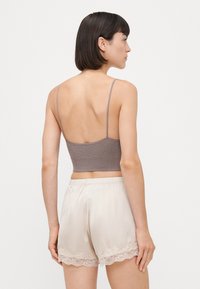 Szary prążkowany crop top na cienkich ramiączkach, zestawiony z kremowymi satynowymi szortami z koronkowym wykończeniem. Widok z tyłu. Gładka faktura i dopasowany krój.